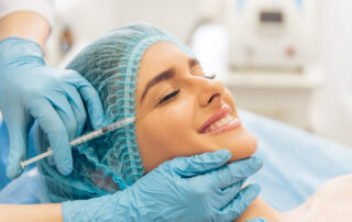 Beautiful young woman is getting an injection in her face and smiling, lying with closed eyes