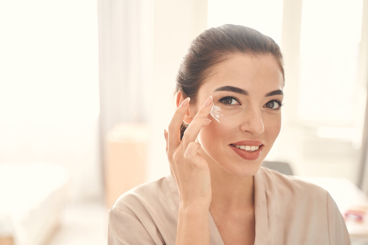 Smiling cheerful lady spending time with beauty procedures at home in the morning while using gentle eye cream